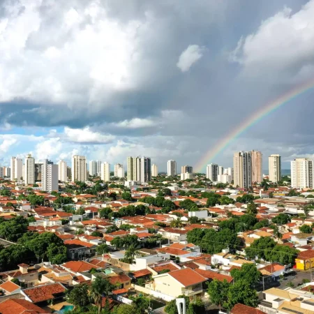 A imagem mostra uma vista panorâmica de Araçatuba, um município brasileiro localizado no interior do estado de São Paulo, com um arco-íris visível no céu sobre a área urbana.